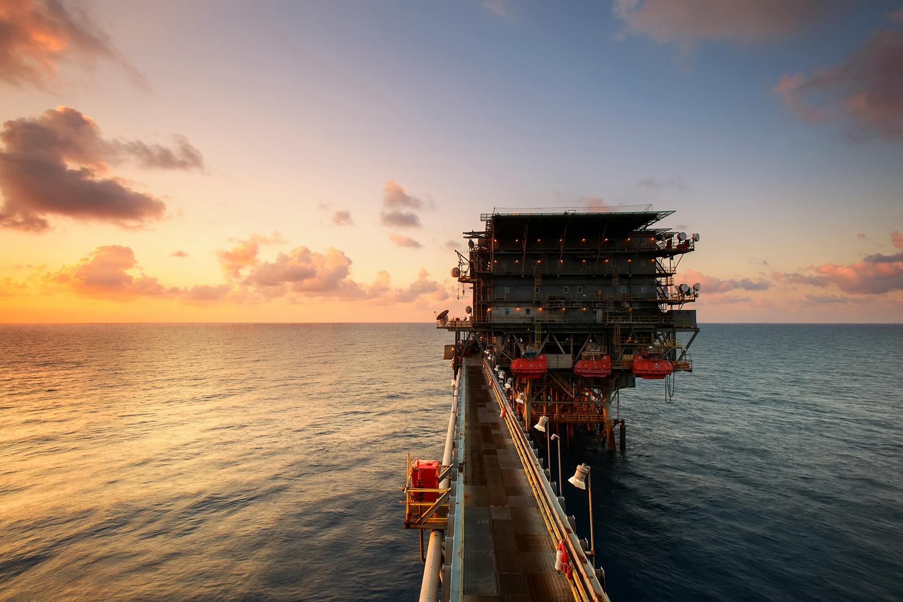 Services A breathtaking view of an oil platform on the ocean at sunset, showcasing industrial beauty.